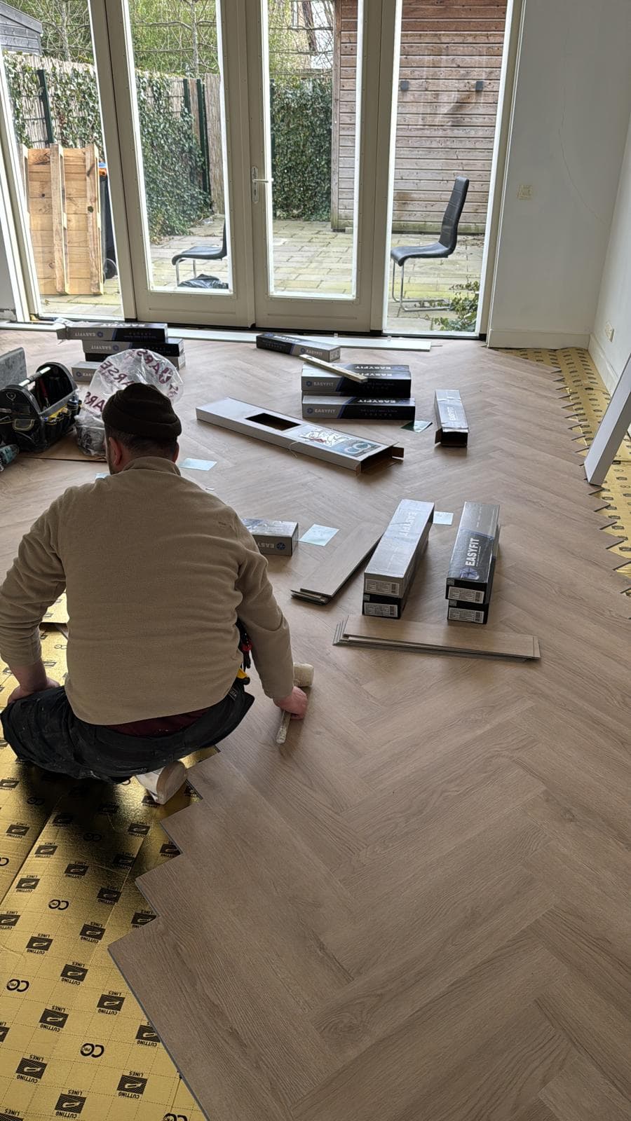 Vakman legt een laminaatvloer in visgraatpatroon in een woonkamer met openslaande tuindeuren